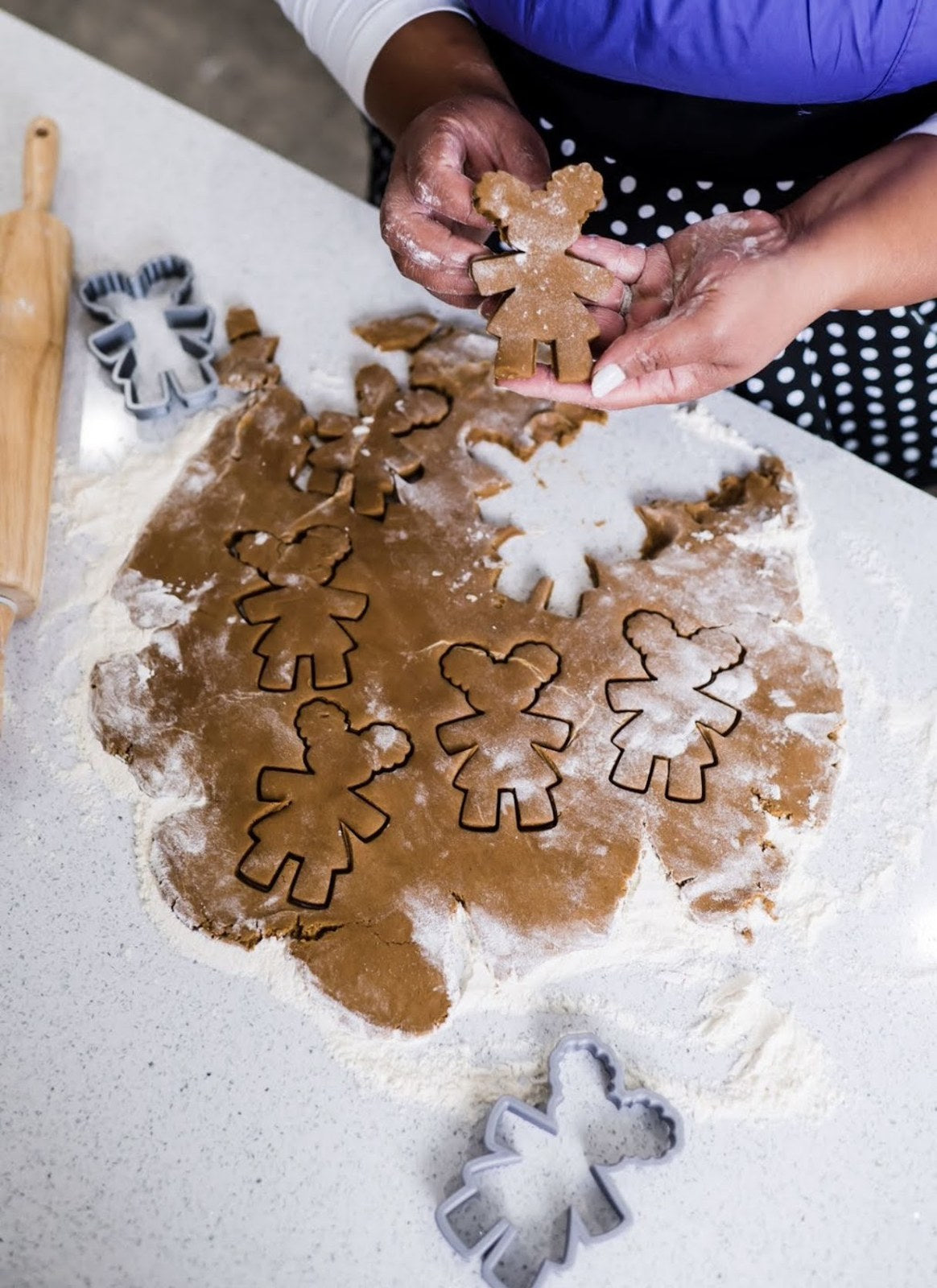 Hands holding a Diva cookie above dough cut into Diva shapes